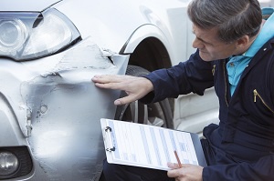Auto Workshop Mechanic Inspecting Damage To Car And Filling In Repair Estimate